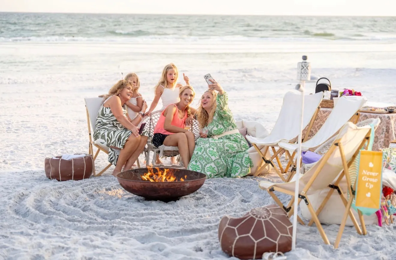 A family taking a casual group selfie by the fire pit on the beach