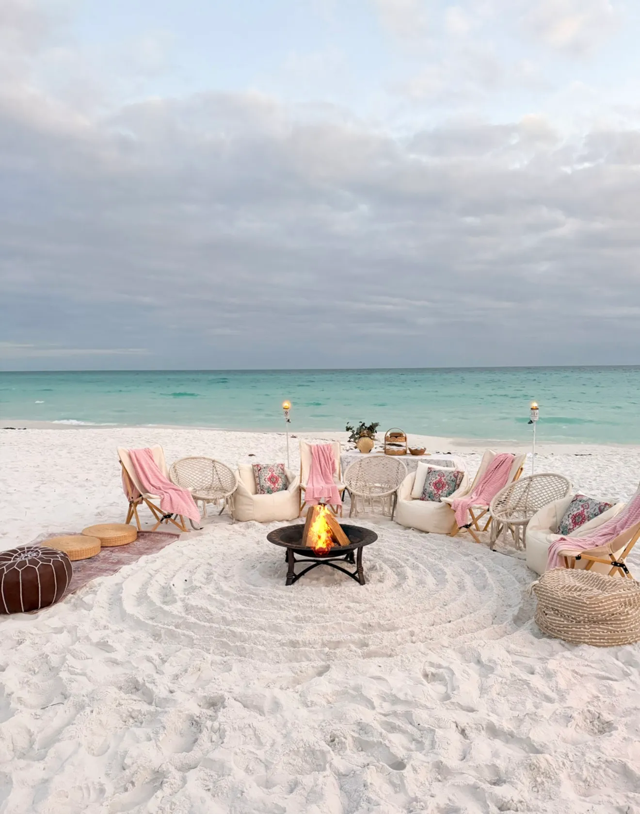 Bonfire lounge seating draped with pink towels facing the Gulf under a cloudy evening sky