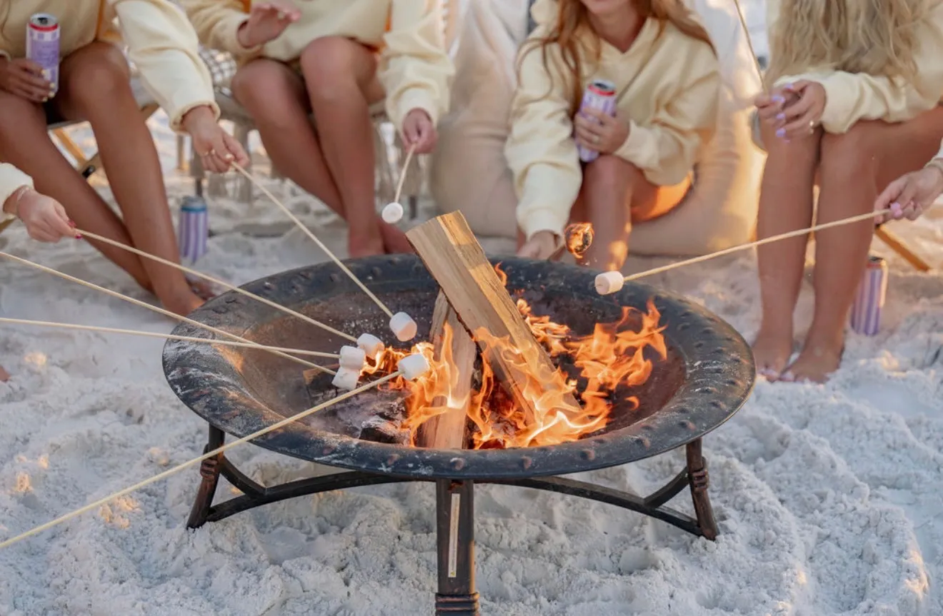 Friends in matching cream sweatshirts roasting marshmallows together over the fire pit