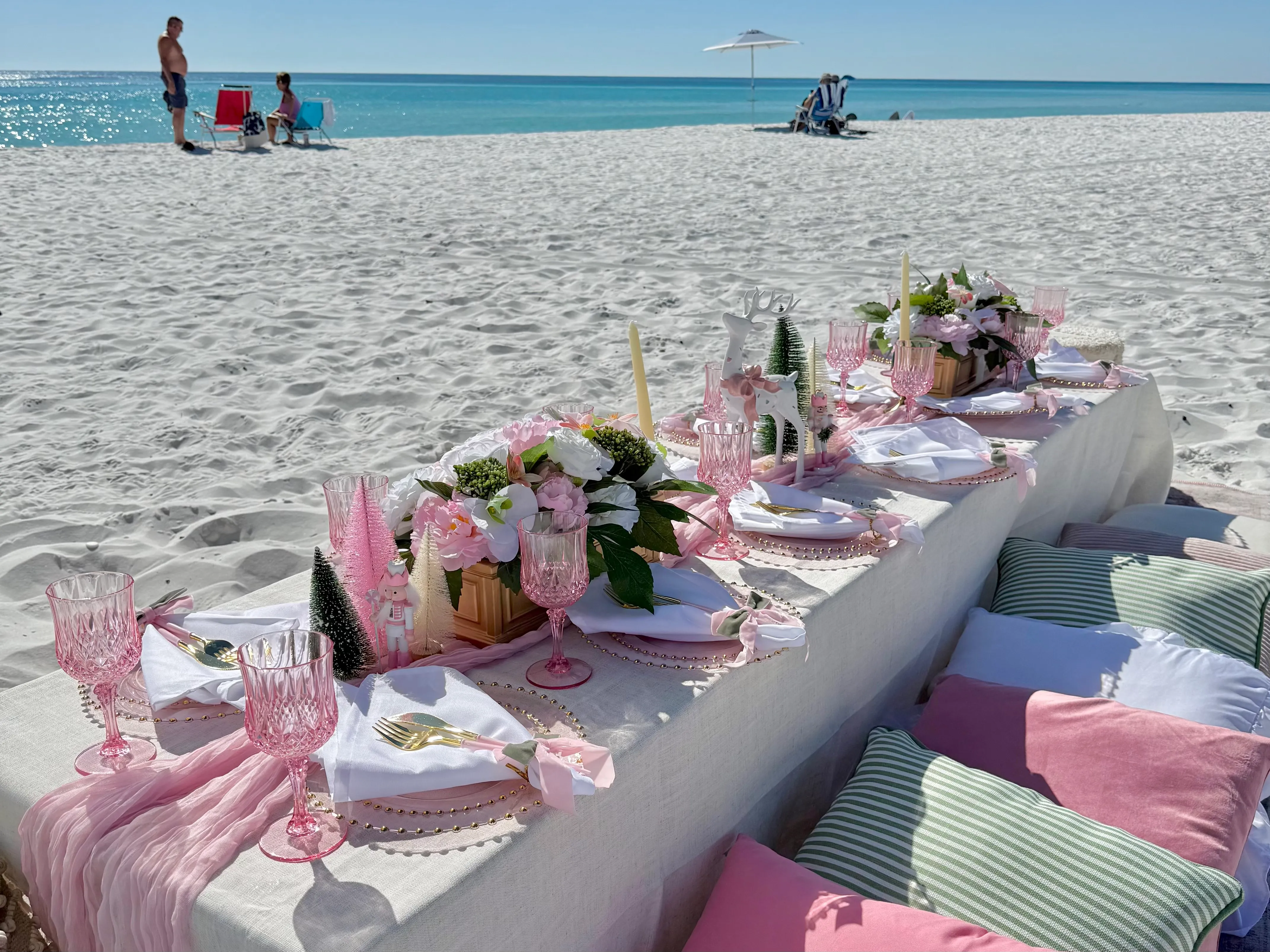 A long beachside table set with a pink and white tablescape, florals, and glassware overlooking the Gulf