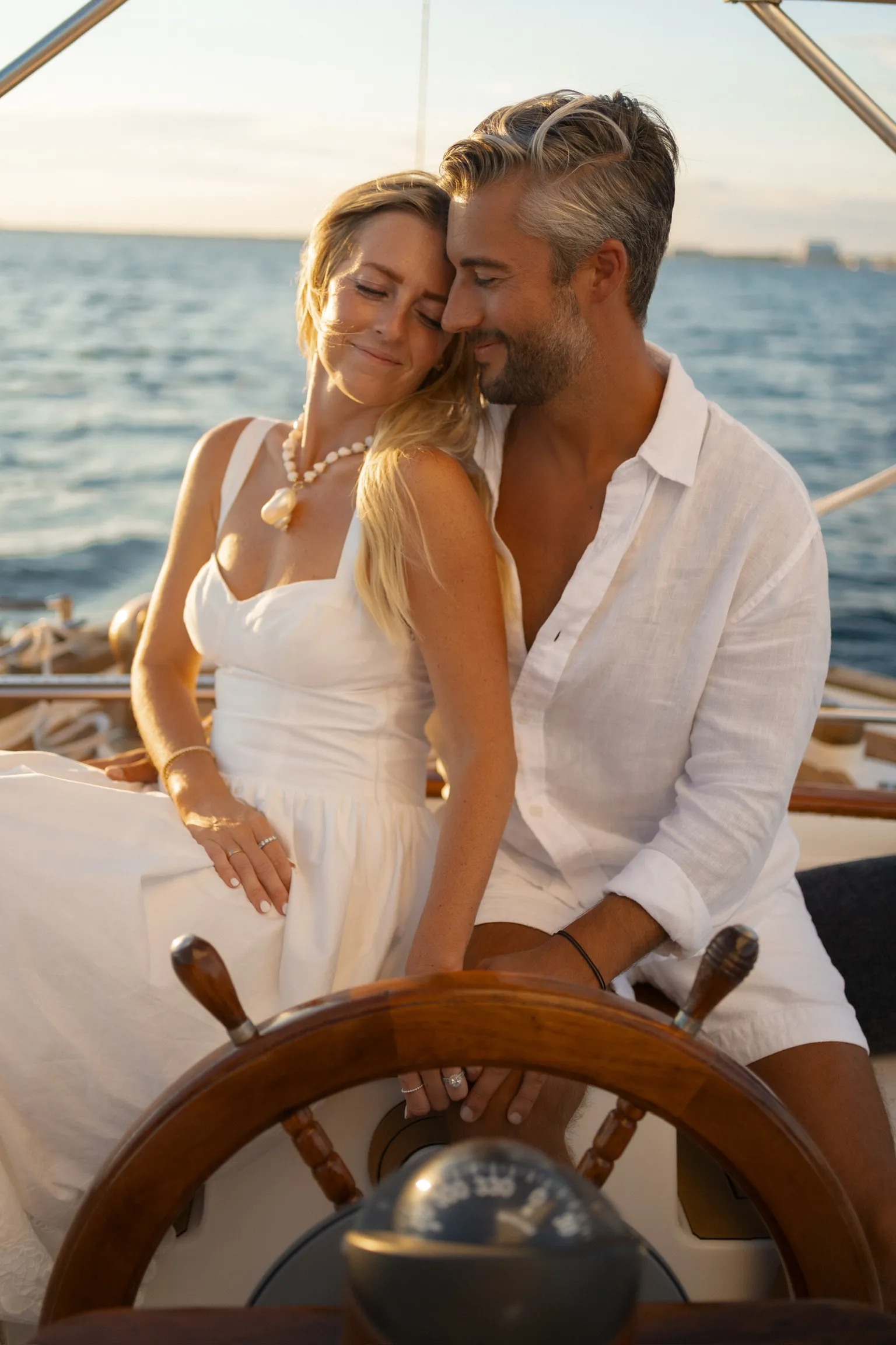 A couple at the ship’s wheel of a sailboat during golden hour
