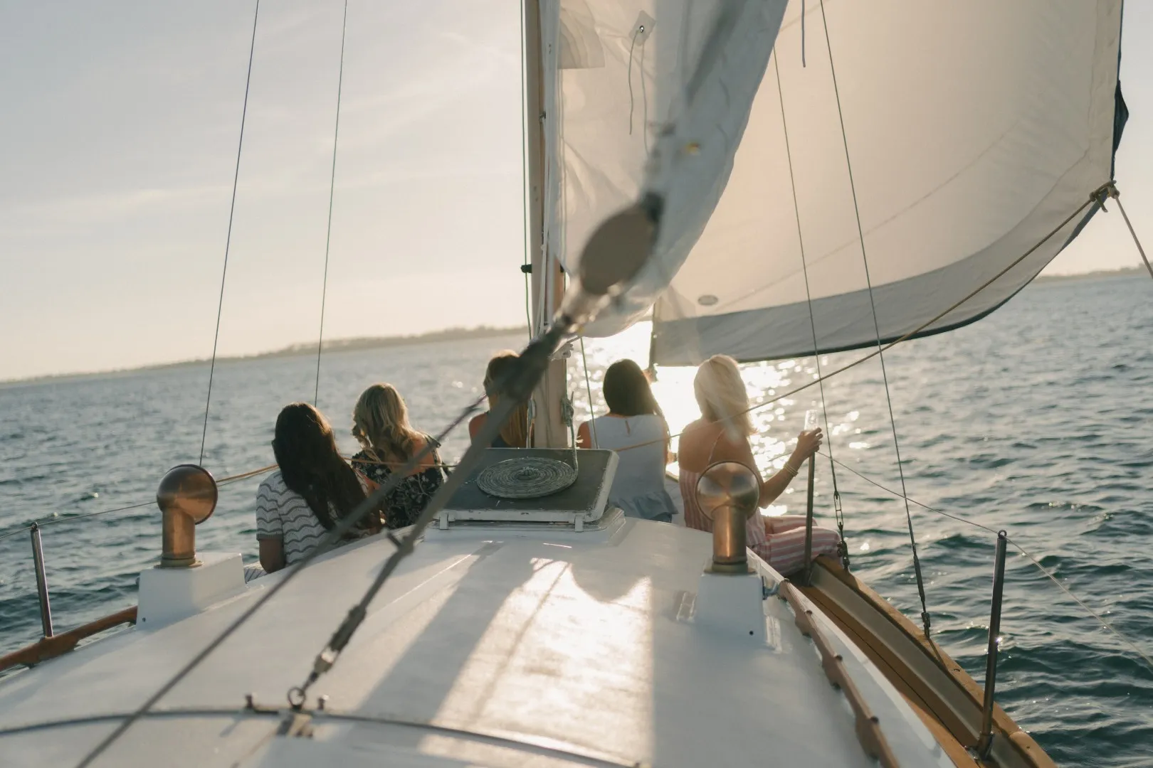 A group of friends seated on the bow of a sailboat watching the sunset over the Emerald Coast