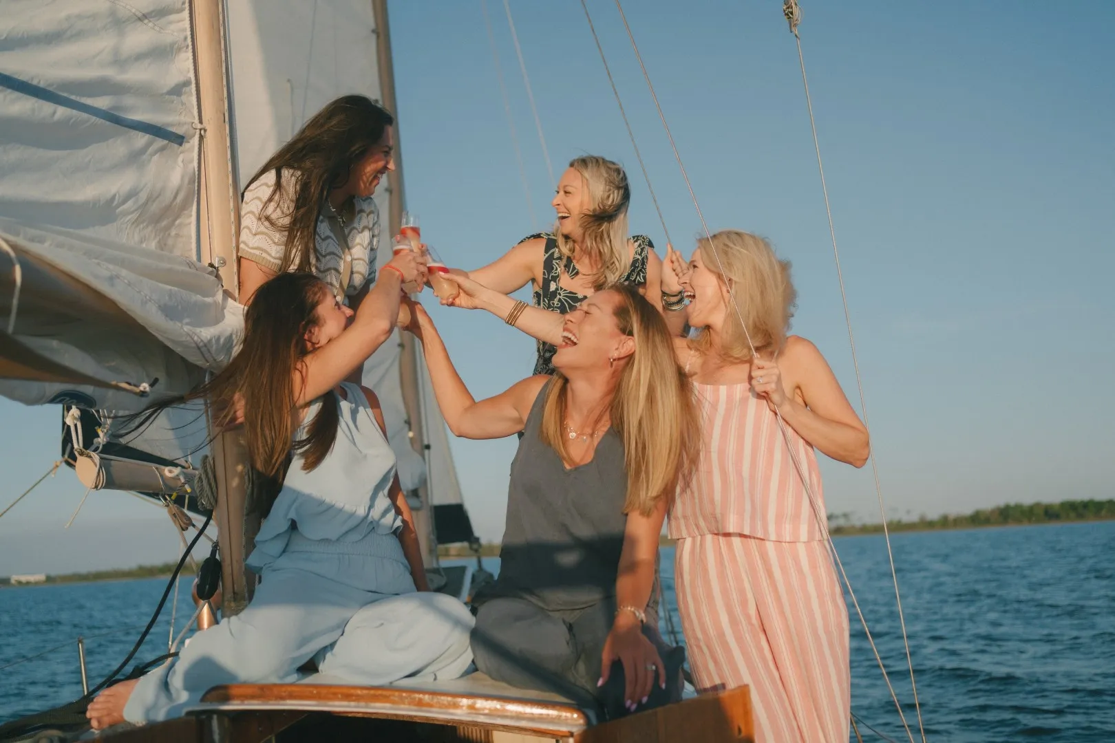 A group of women raising a toast on the deck of a sailboat at golden hour